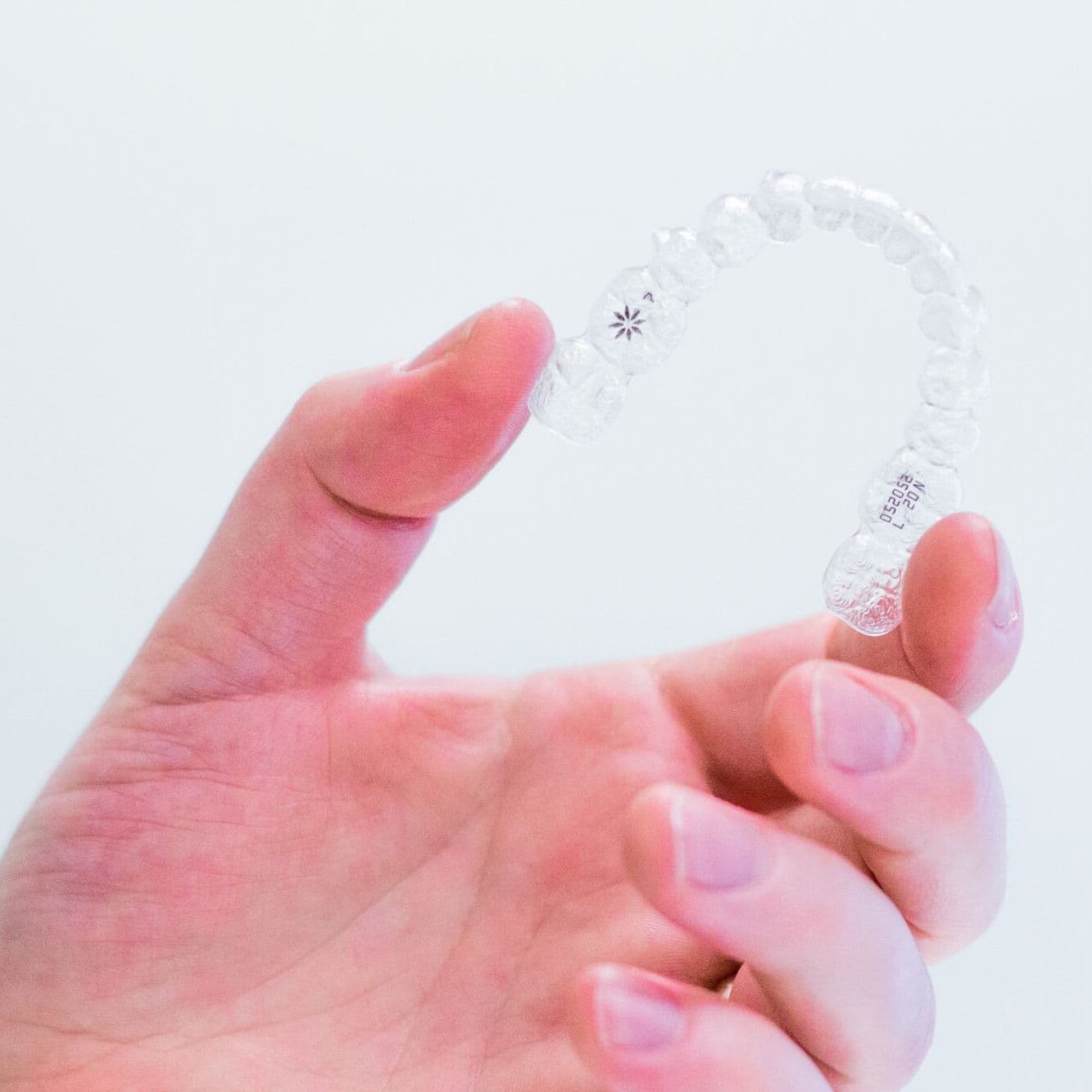 Hand holding a clear Invisalign aligner, showcasing its transparent design, relevant to orthodontic treatment options at Smiles From the Hart.