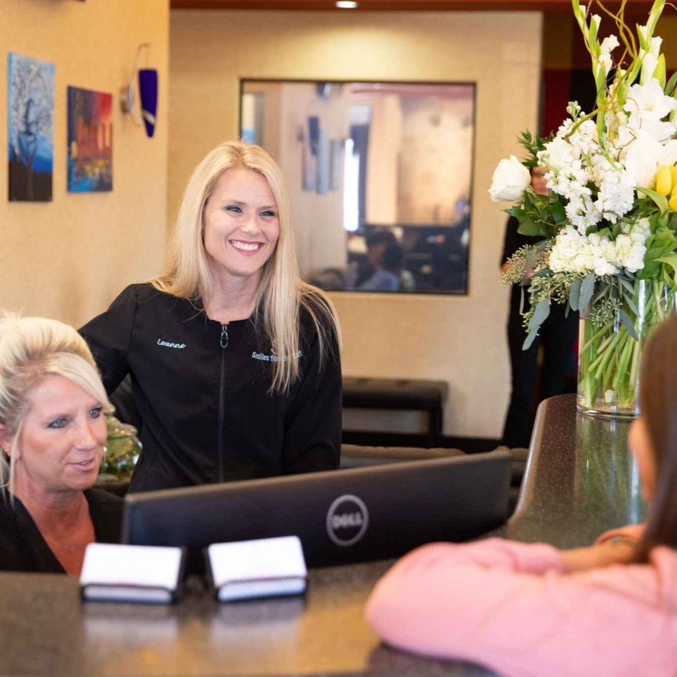 Receptionists at Smiles from the Hart orthodontic practice assisting a patient, with a welcoming environment and floral arrangement in the background.