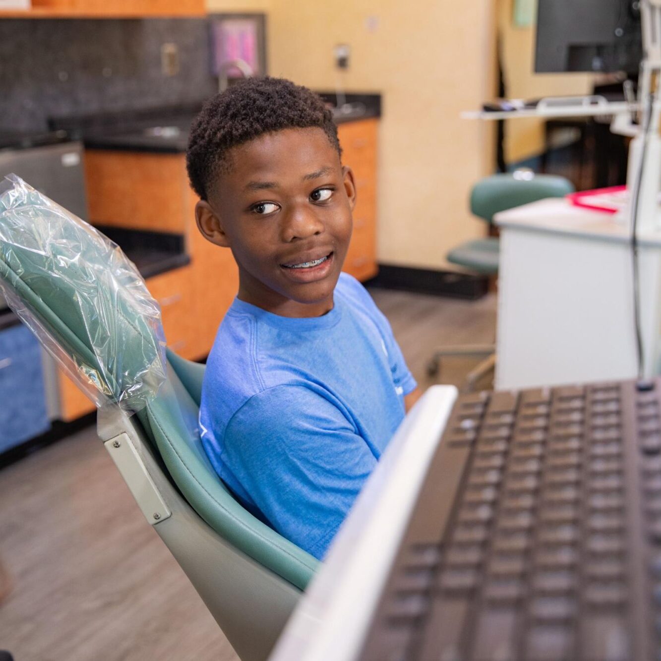 Young boy in orthodontic chair smiling, wearing braces, in a dental office setting with modern equipment and warm colors, reflecting a welcoming atmosphere for patients at Smiles from the Hart Orthodontics.