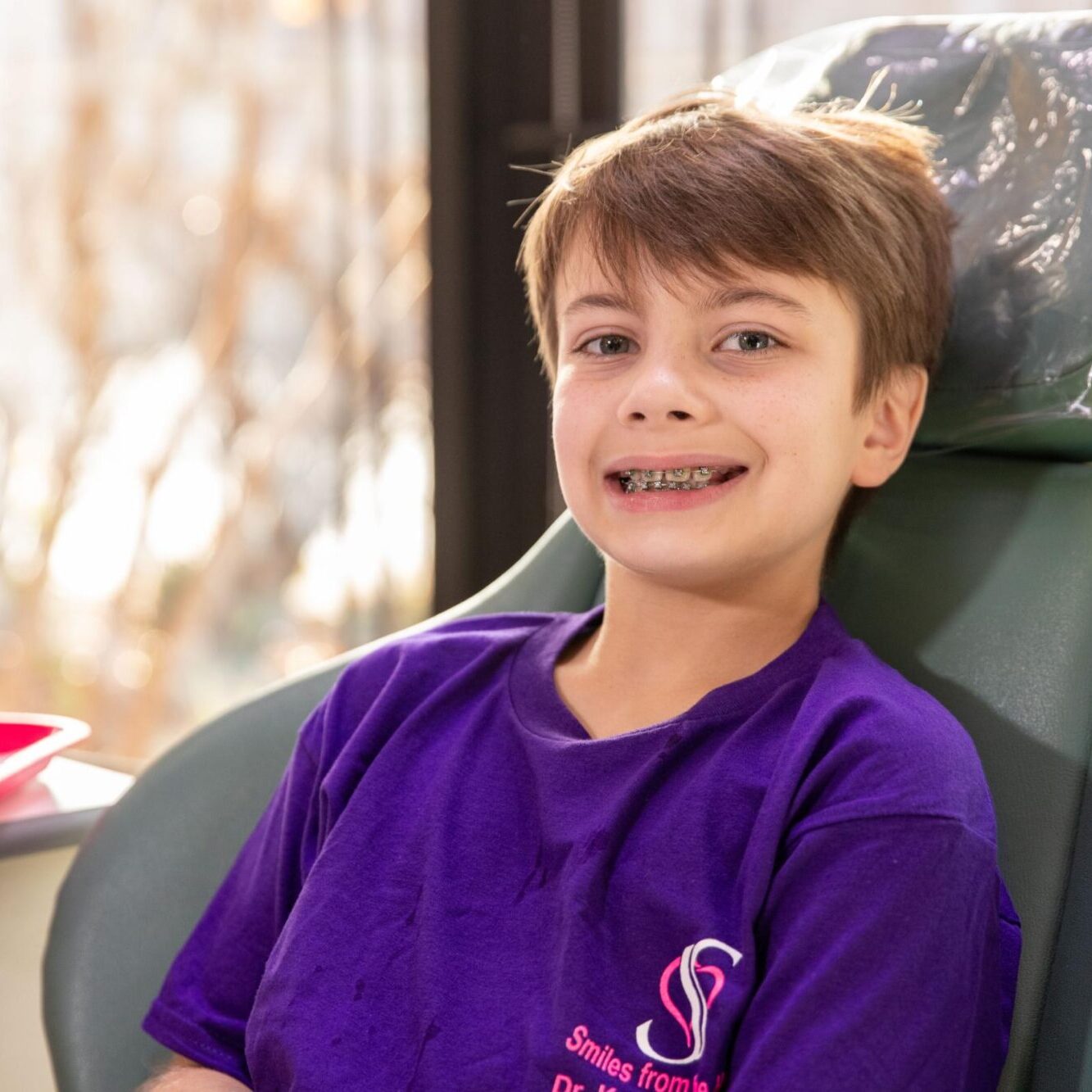 Child in orthodontic chair wearing purple Smiles from the Hart t-shirt, relaxed atmosphere in orthodontic office.