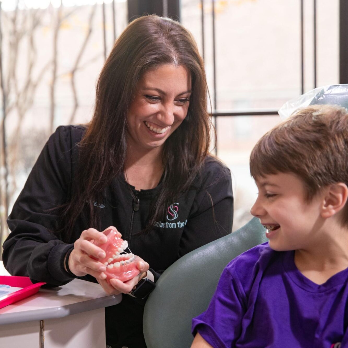 Orthodontic consultation at Smiles from the Hart, staff demonstrating dental model to child, highlighting braces and treatment options.