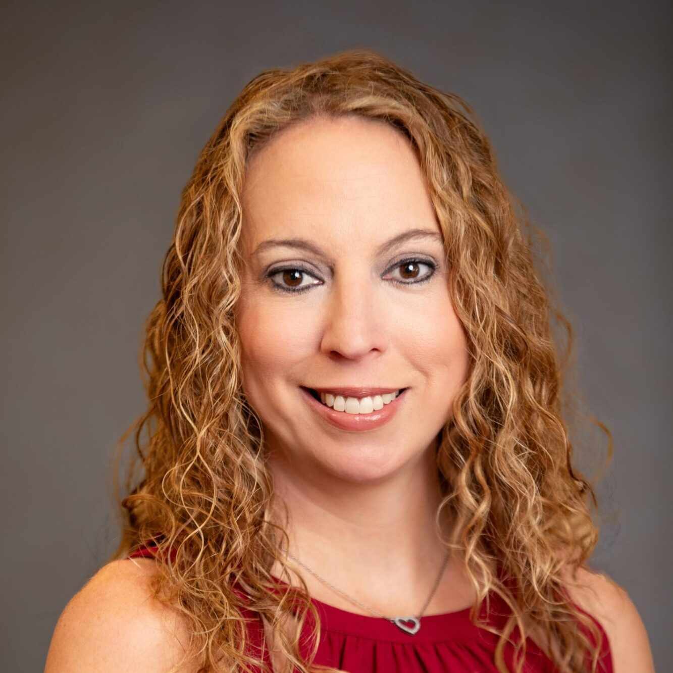 Dr. Katherine A. Hart Westphal, orthodontist at Smiles from the Hart, smiling warmly in a red top against a neutral background, emphasizing her dedication to personalized orthodontic care in Murfreesboro, TN.